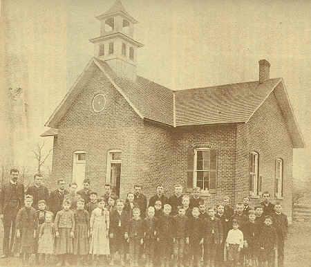 An old photo of a schoolhouse with people grouped for the photo.