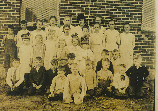 Teachers and schoolchildren lined up for the class photo in front of a brick schoolbuilding.