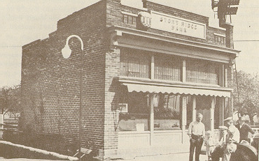 Two men and a child outside a brick building that has a sign reading "Stony Ridge Bank."
