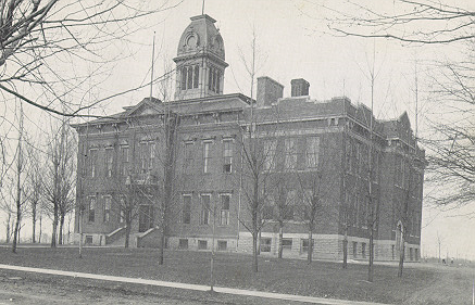 Black and white photos of a brick schoolbuilding surrounded by trees with no leaves.