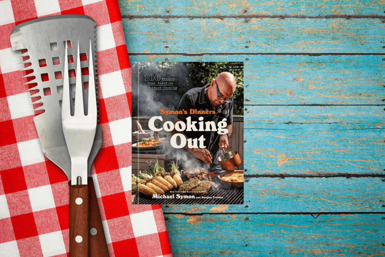 July's cookbook, Cooking Out, on a wooden table next to cooking instruments.