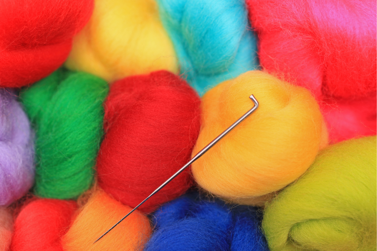 A felting needle lies atop colorful yarns of wool.