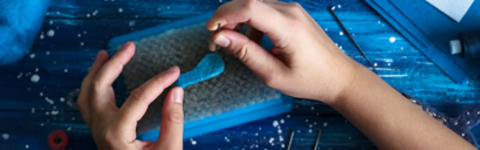 hands needle felting a blue whale on a sponge.