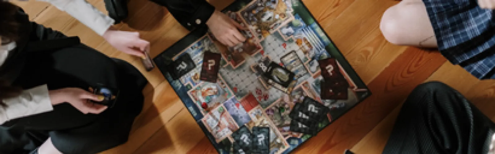 A group sits together and plays a board game on a wooden floor.
