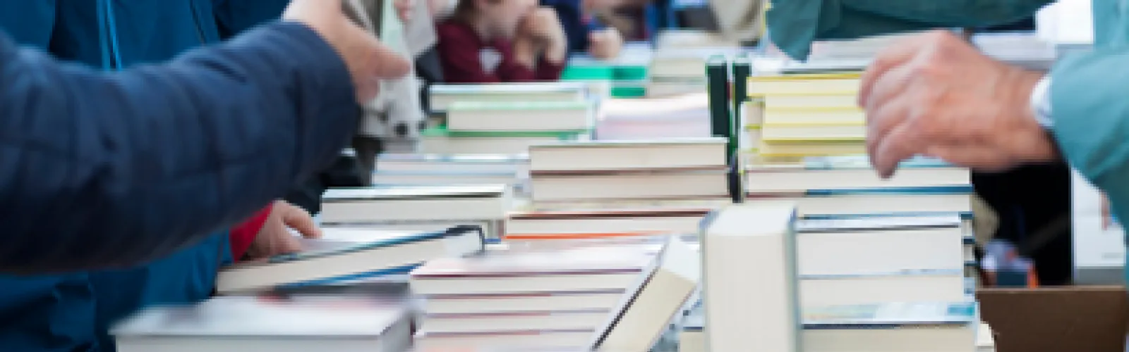 books in rows on a table with people looking to buy them.
