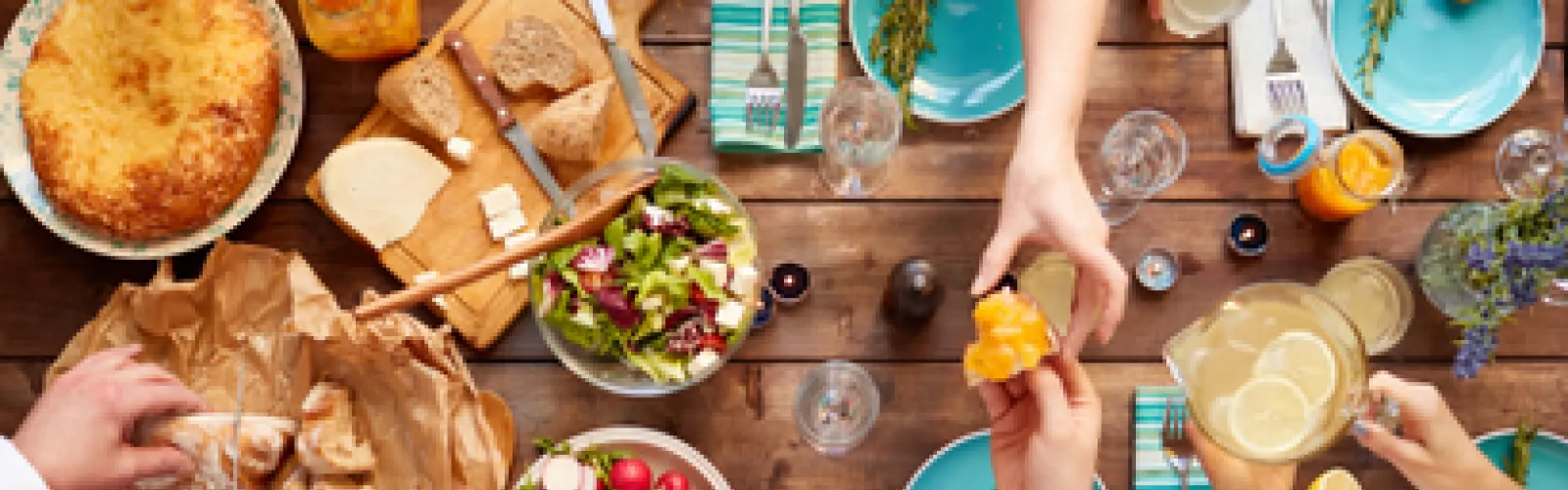 A top-down view of a table with an assortment of food and various people preparing it.